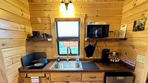 Una cocina compacta con paredes de madera, un lavamanos, un microondas y un refrigerador.