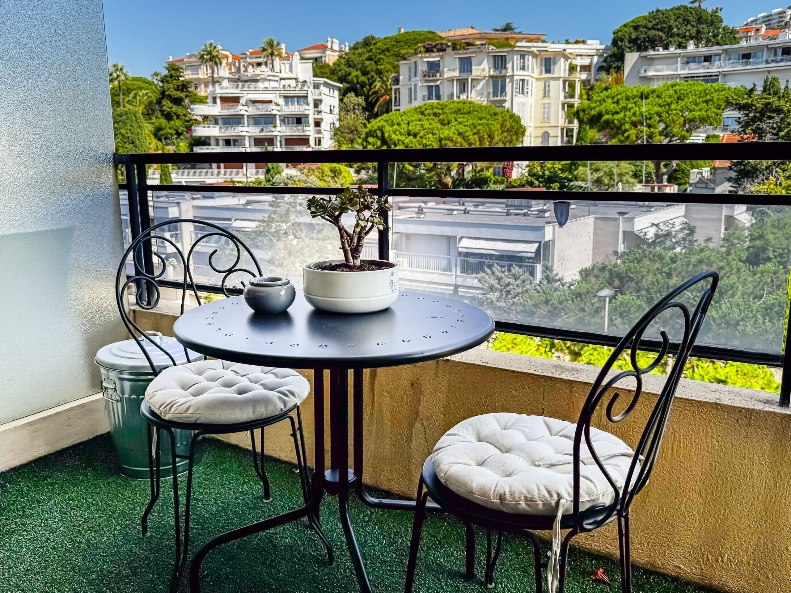 Un balcon avec une table ronde, deux chaises, un pot de fleurs et une théière.