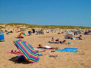 Ein Strand mit sonnenbadenden Personen, Zelten und bunten Sonnenschirmen.