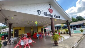 Un área de estar al aire libre techada con mesas y sillas, un cartel que dice 'D'Mama Chalet' y una piscina al fondo.