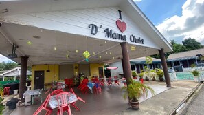 Un área de estar al aire libre techada con mesas y sillas, un cartel que dice 'D'Mama Chalet' y una piscina al fondo.