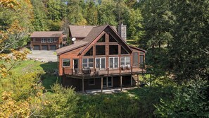 A two-story wooden cabin with a balcony, surrounded by dense forest. - Zen Den • Sleeps 14 • 40-Acre Berkshire Retreat (Stephentown)