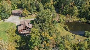 Ein großes Haus mit einer Terrasse, umgeben von dichtem Wald und einem Teich.