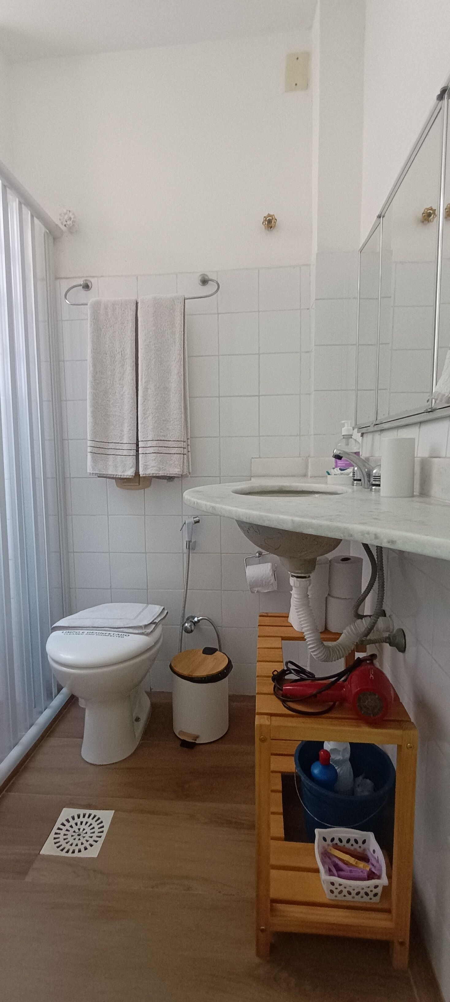 A bathroom with a toilet, sink, and a small wooden cabinet with a trash bin.