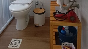 Et badeværelse med toilet, håndvask og et lille træskab med skraldespand.