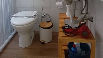 A bathroom with a toilet, sink, and a small wooden cabinet with a trash bin.