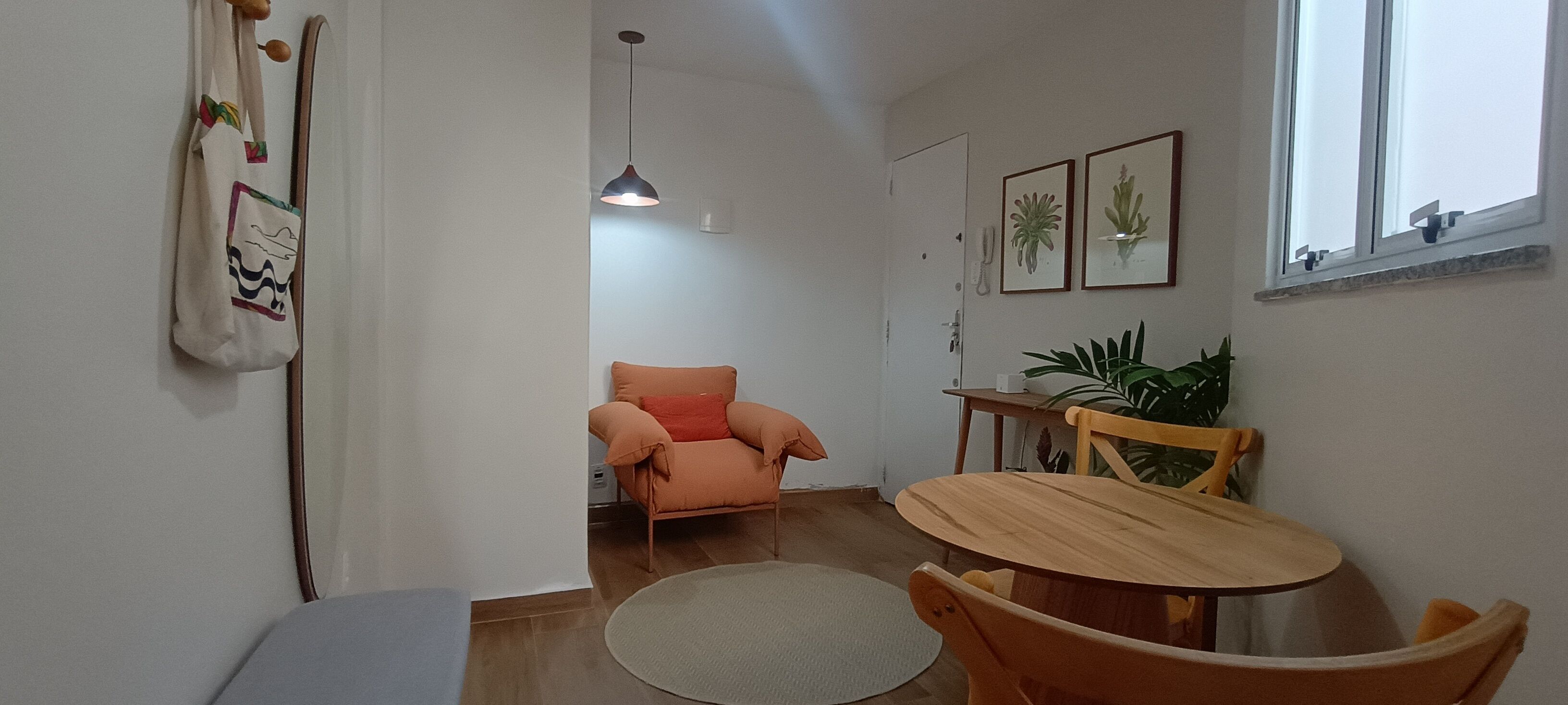 Une pièce comprenant une table à manger, des chaises, un canapé, un luminaire suspendu et une fenêtre avec une plante.