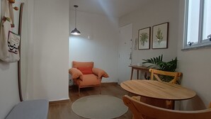 Et værelse med spisebord, stole, sofa, en hængende lampe og et vindue med en plante.