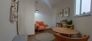 Une pièce comprenant une table à manger, des chaises, un canapé, un luminaire suspendu et une fenêtre avec une plante.