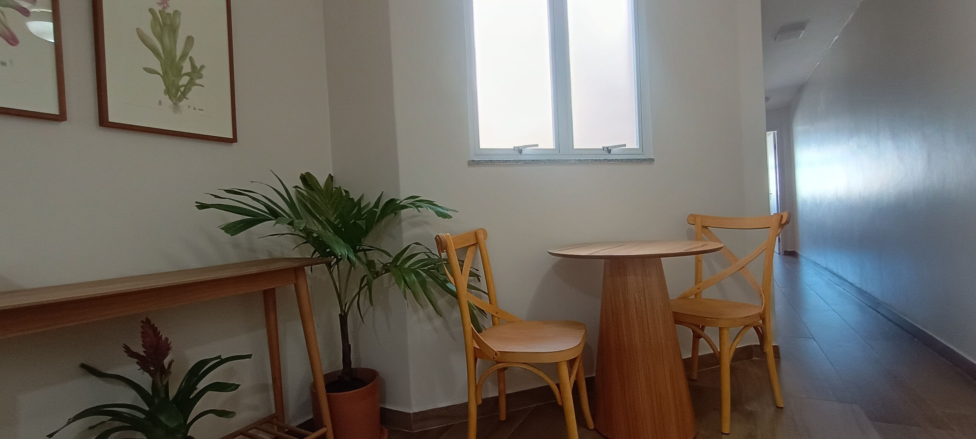 Un couloir avec une chaise en bois et une petite table, une plante en pot et une fenêtre laissant entrer la lumière naturelle.