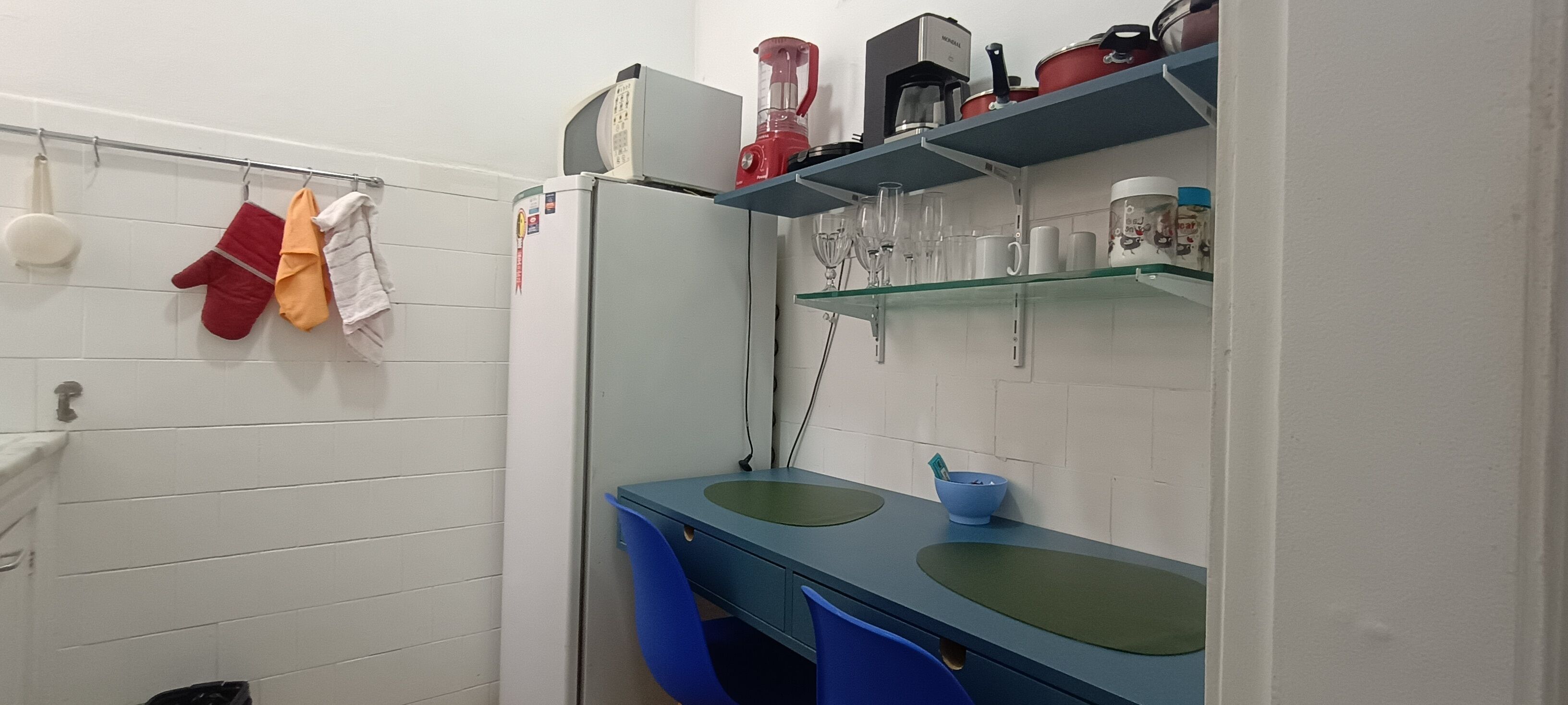 Une salle de bain avec un mur recouvert de carreaux blancs, un lavabo bleu et une étagère contenant divers objets, dont un appareil électroménager rouge.