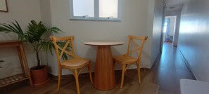 Ein Zimmer mit einem Holztisch, zwei Stühlen, einer Topfpflanze und einem Fenster.