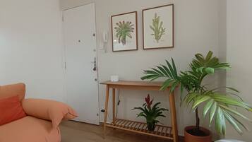 A room with a sofa, a wooden side table with a potted plant, and two framed botanical illustrations on the wall.