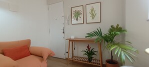 Ein Zimmer mit einer Couch, einem Holztisch mit einer Topfpflanze und zwei gerahmten Pflanzenabbildungen an der Wand.