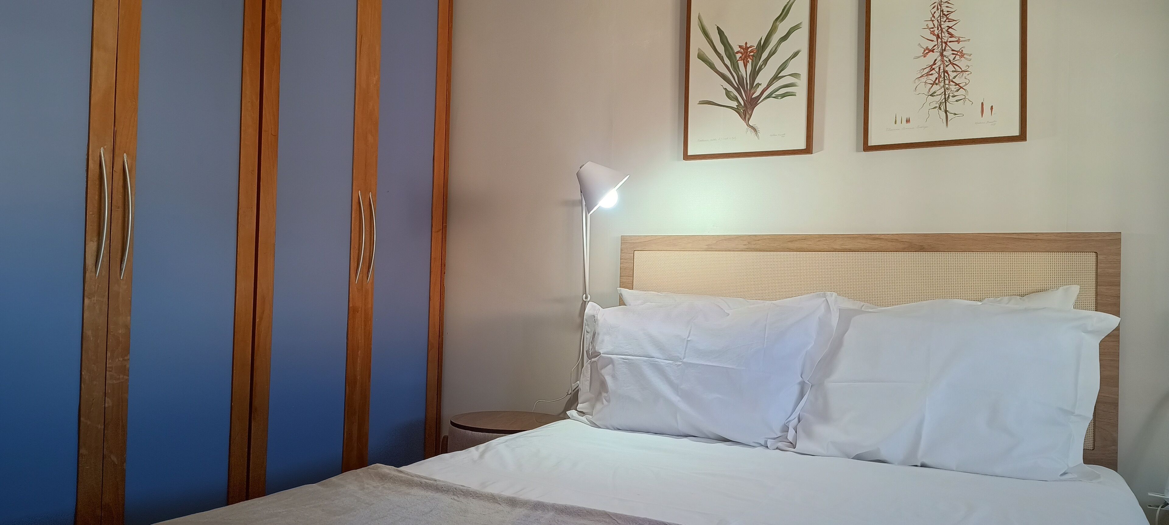 Une chambre à coucher avec un lit, une armoire en bois et deux illustrations botaniques encadrées accrochées au mur.