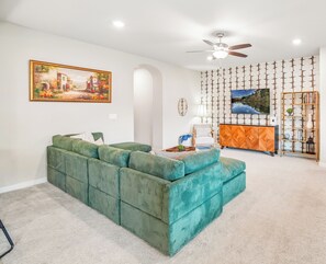 A living room with a green sofa, a painting, a ceiling fan, and a patterned wall.