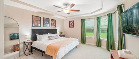 Un dormitorio con cama, ventilador de techo, televisor, espejo y un cuadro en la pared.