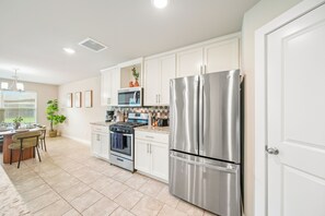A modern kitchen with white cabinetry, stainless steel appliances, and a dining area with a table and chairs.