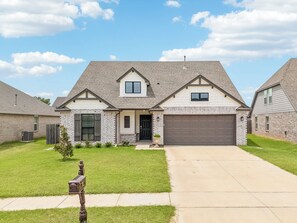 A two-story house with a front garage, a small front porch, and a well-maintained lawn. - Sleeps 7~GarageAccess~Coffee Bar~Patio w/ FirePit (Bixby)