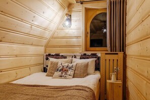 A wooden cabin bedroom with a bed, a window, and a wooden door.