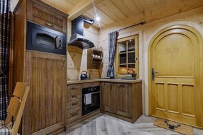 Een houten interieur met een ingebouwde oven, een deur met een hartmotief en een raam met gordijnen.