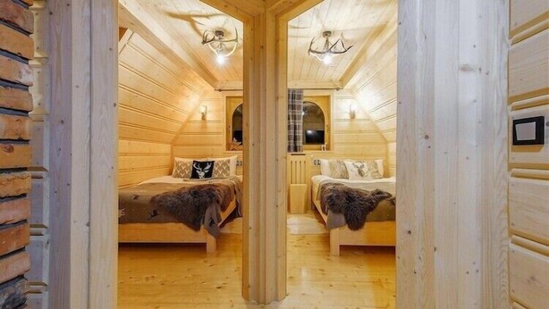 Ein Holzinnenraum mit zwei Betten, einem Kamin und einer Holzbalkendecke.