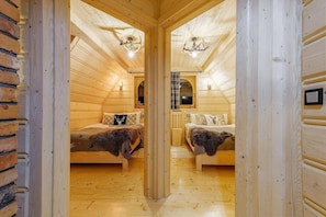 A log cabin interior with two beds, a fireplace, and a wooden ceiling.