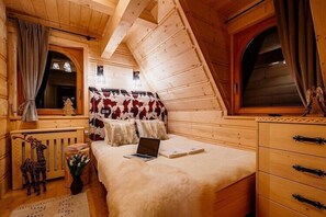 Quarto de cabana de madeira com cama, um laptop, cômoda e janela com cortinas.