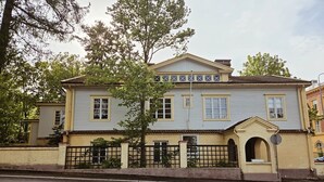 A two-story building with a symmetrical facade, a central entrance with an archway, and a gated front yard. - Historic Pyynikki 3BR Apt Free Parking (Tampere)