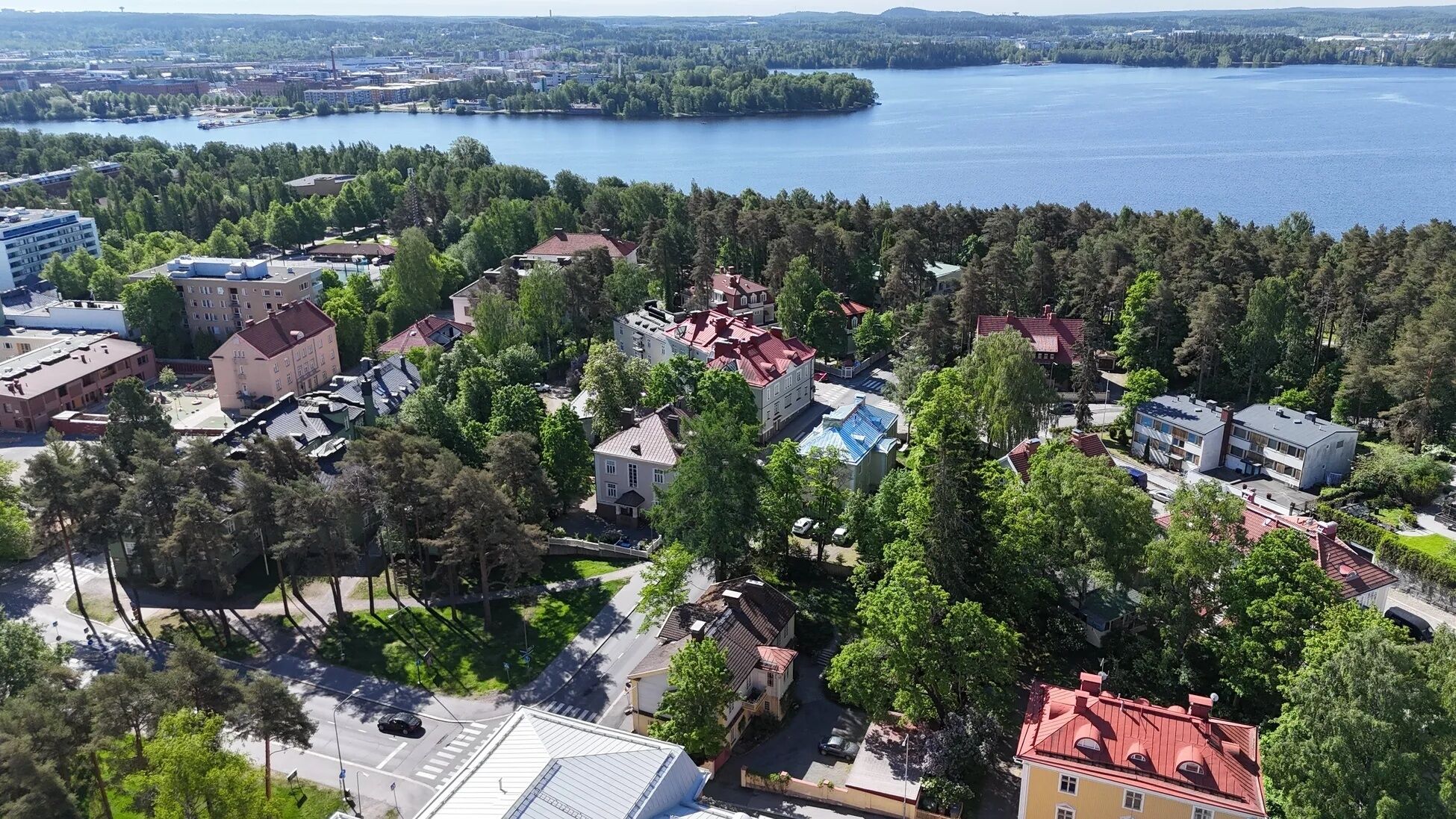 An aerial view of a residential area with buildings surrounded by trees and a lake in the background.