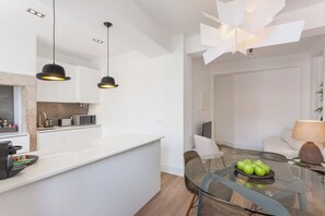 A modern kitchen with white cabinetry, a glass dining table with chairs, and pendant lighting. - Your Lisbon Home Santa Apolónia (Lisbon)