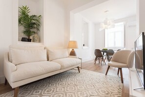 Ein modernes Wohnzimmer mit einer Couch, einem Esstisch mit Stühlen, einer Lampe und einem Fernseher.