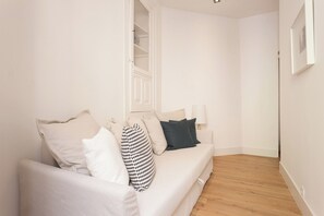 A minimalist living room with a white sofa, a wooden floor, and a white door leading to a closet. - Your Lisbon Home Santa Apolónia (Lisbon)