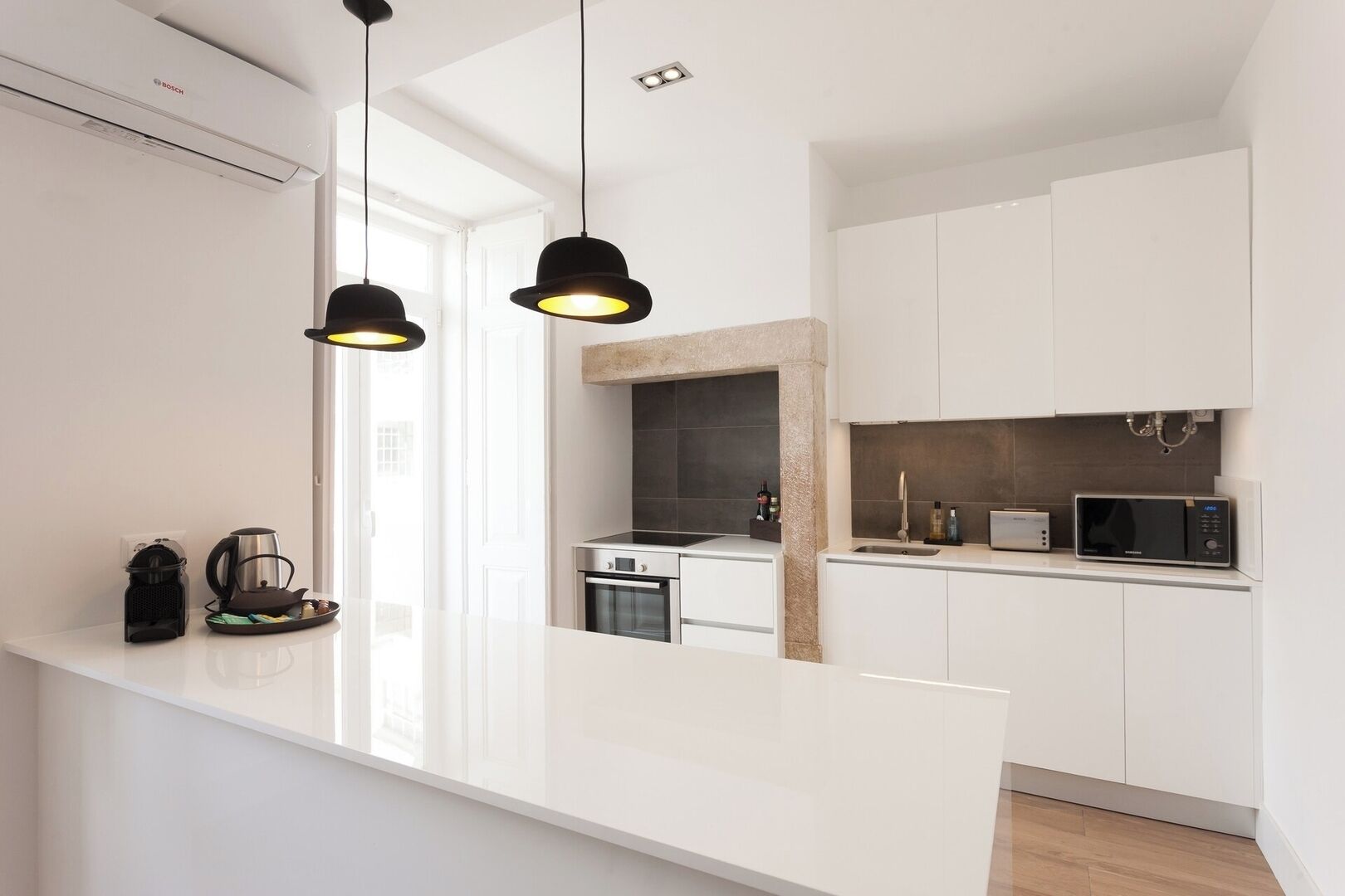 Una cocina moderna con armarios blancos, horno empotrado, microondas e iluminación colgante.