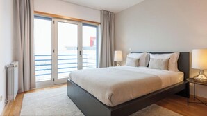 Et hotelværelse med en stor seng, to sengeborde med lamper, udsigt gennem en glasdør og et lille bord.