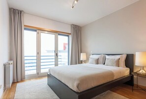 Hotellihuone, jossa on suuri sänky, kaksi yöpöytävalaisinta, näkymä lasiovesta ja pieni pöytä.