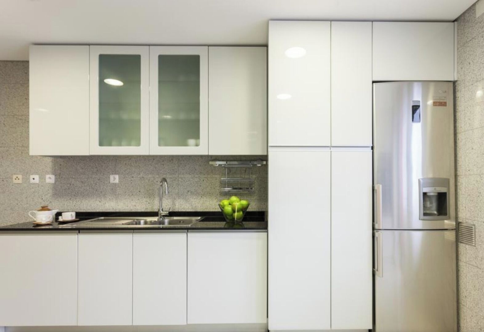 Una cocina moderna con armarios blancos, un refrigerador de acero inoxidable y una encimera de granito.
