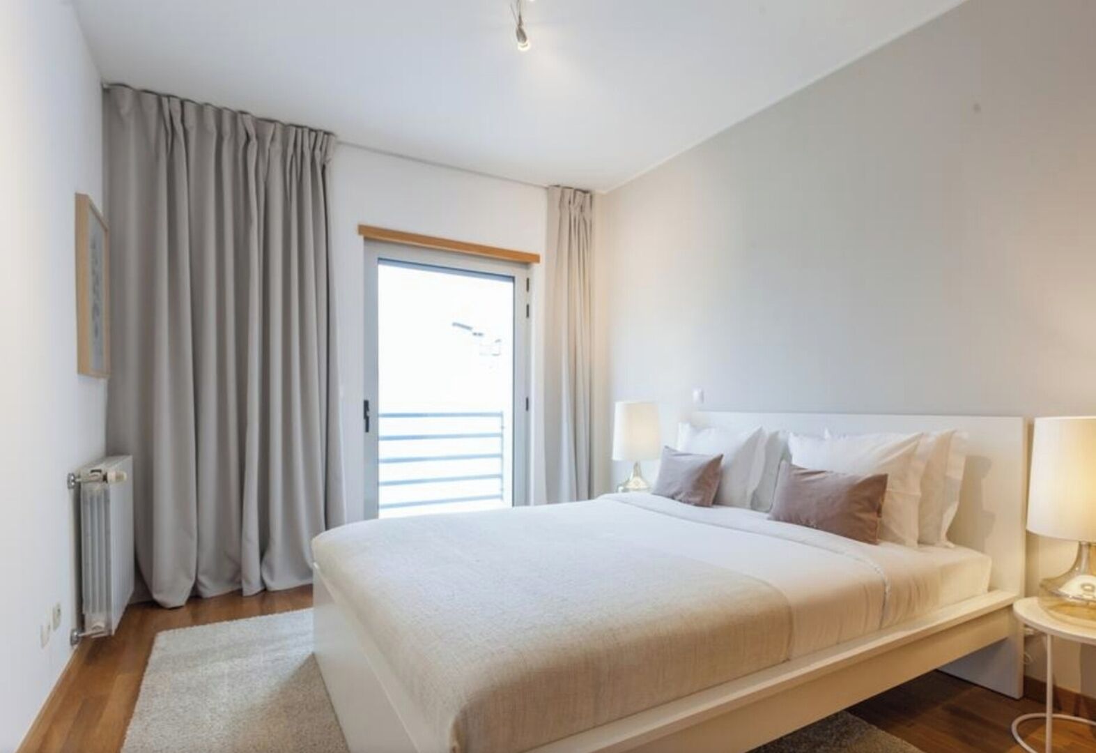 A hotel room with a bed, bedside lamps, a window with curtains, and a radiator.