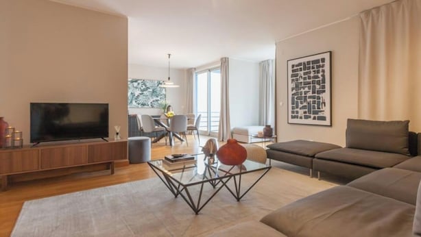 En moderne stue med et fladskærms TV, et glasbord, en sofa og et spiseområde med stole.