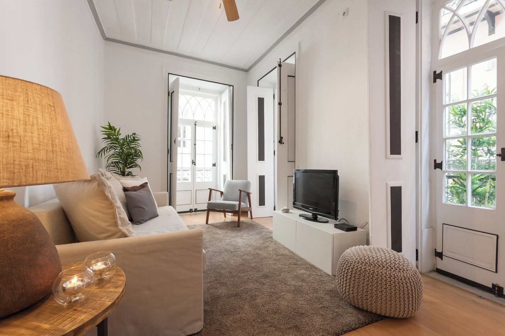 A living room with a sofa, a television, a lamp, a plant, and a door leading to another room.