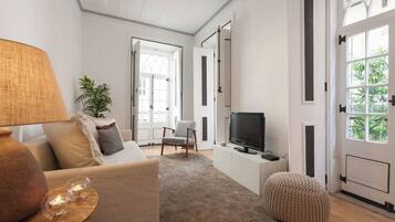 A living room with a sofa, a television, a lamp, a plant, and a door leading to another room.