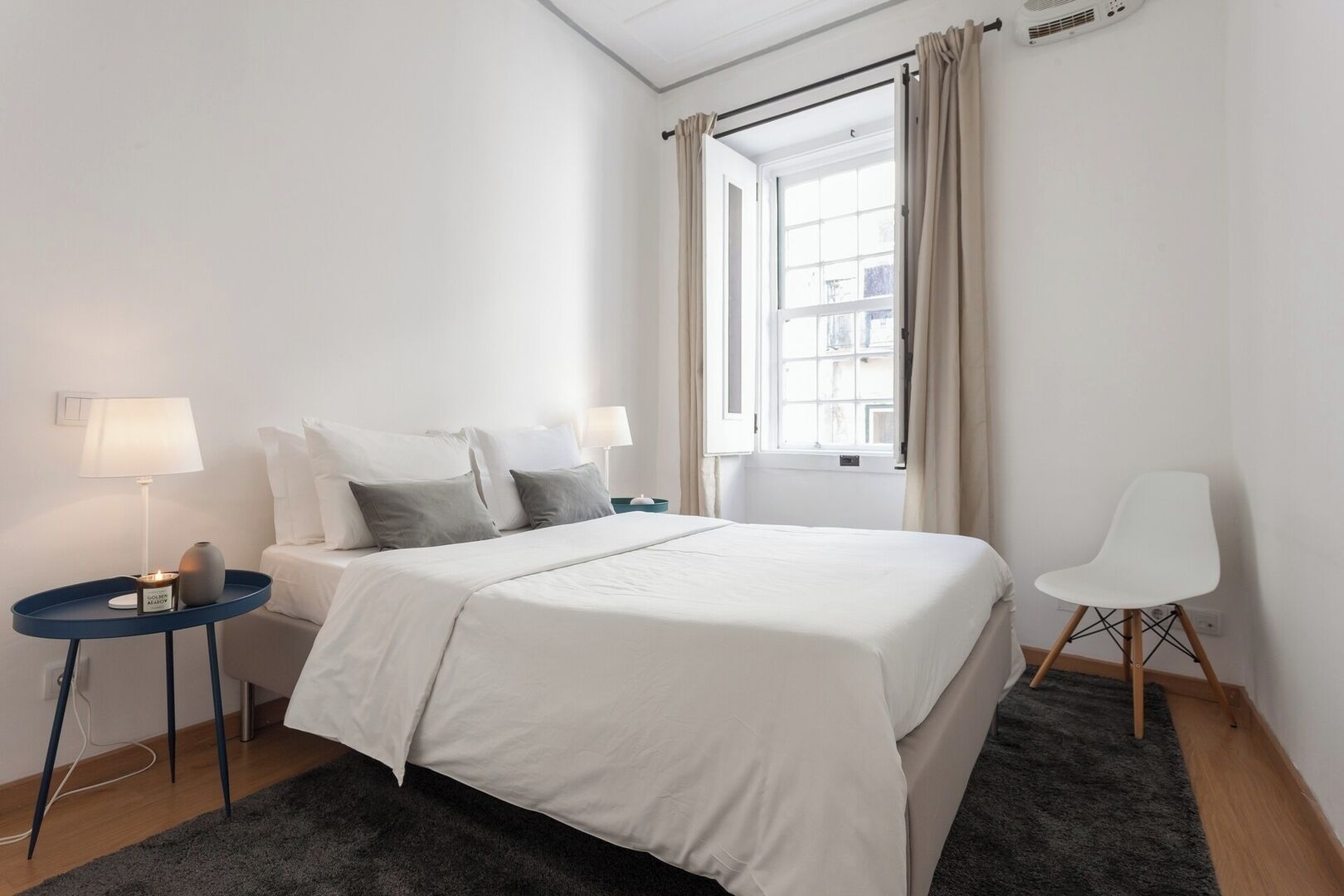 A hotel room with a bed, two bedside tables with lamps, a chair, and a window with curtains.