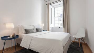 A hotel room with a bed, two bedside tables with lamps, a chair, and a window with curtains.
