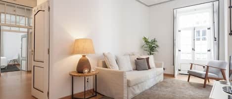 Una sala de estar moderna con un sofá blanco, una mesita redonda de madera con una lámpara, una planta en maceta y un ventilador de techo.