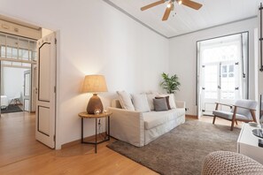 A modern living room with a white sofa, a round wooden side table with a lamp, a potted plant, and a ceiling fan. - Casa da Rua do Norte - 5 Bedroom Apartment (Lisbon)