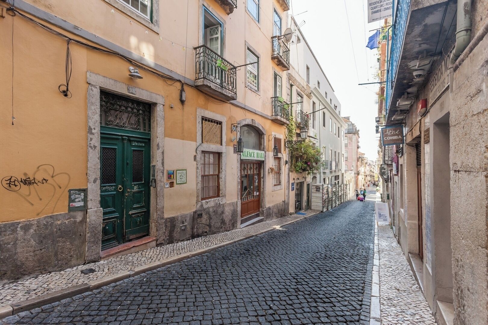 A narrow cobblestone street lined with buildings, some with balconies and signage.