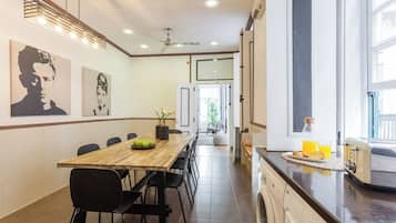 Une cuisine moderne équipée d’un lave-linge intégré, un coin repas avec une longue table et des chaises, et des œuvres d’art accrochées aux murs.