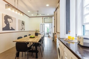 A modern kitchen with a built-in washing machine, a dining area with a long table and chairs, and artwork on the walls. - Casa da Rua do Norte - 5 Bedroom Apartment (Lisbon)
