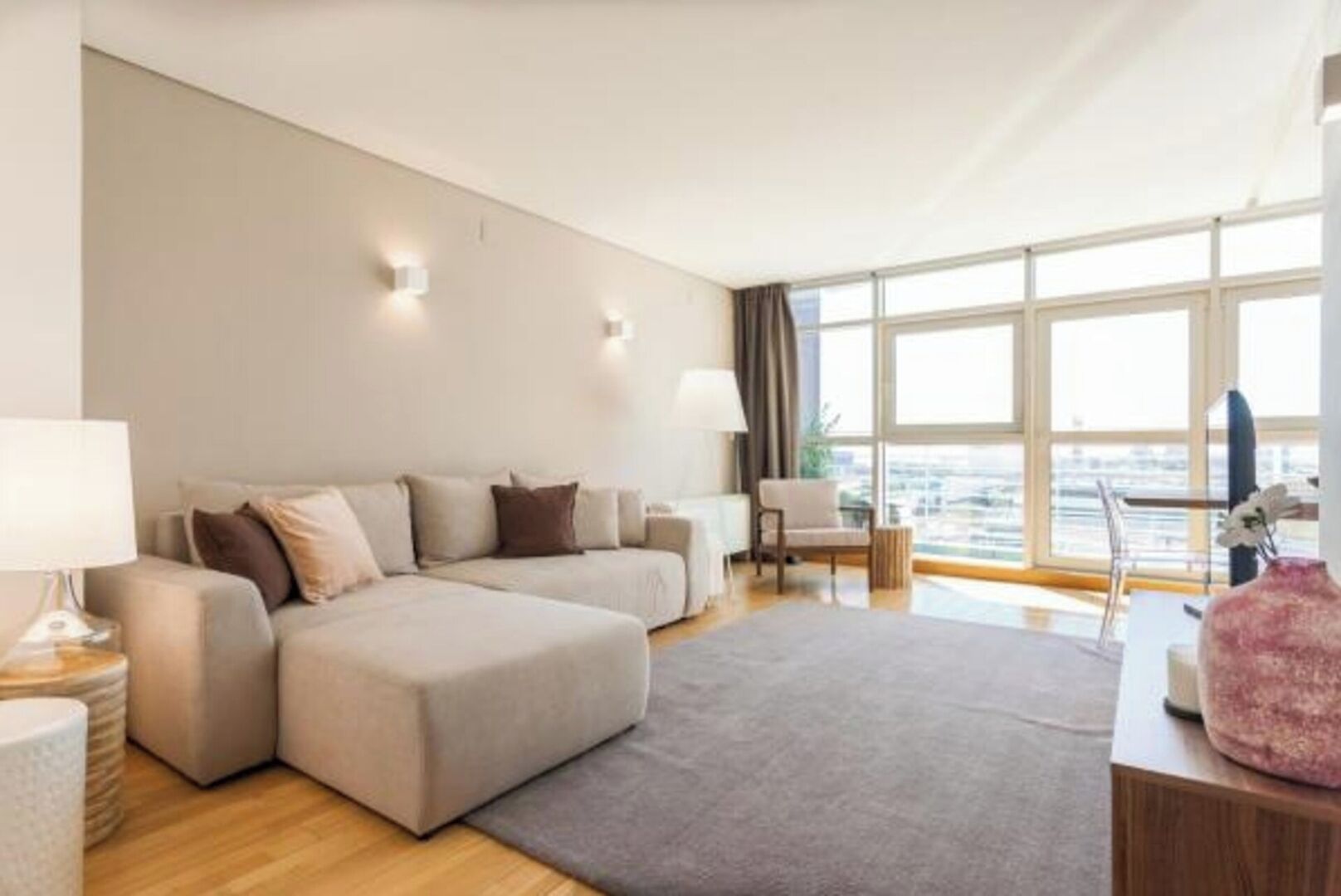 Un salon moderne avec un canapé d’angle, une petite table et une vue sur la ville grâce à de grandes fenêtres.