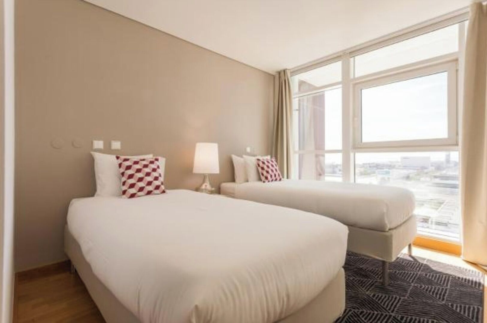A hotel room with two beds, a window with curtains, and a patterned rug.